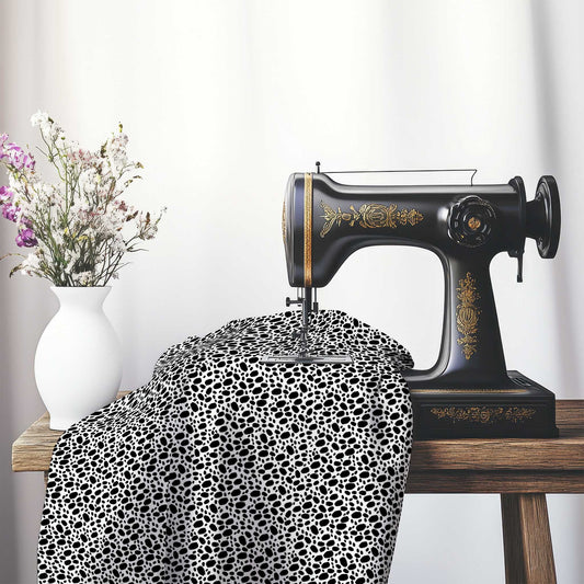 Off-White Cotton Sateen Fabric with Black Hand-painted Dab Motif Print, FASC-1010-092, on an antique sewing machine sitting on a desk with vase of beautiful flowers.