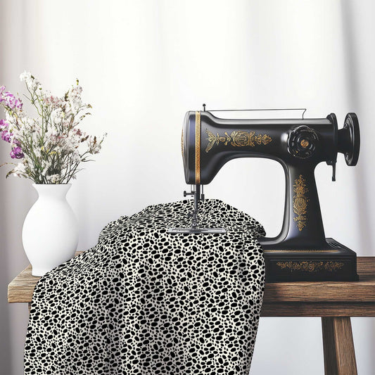 Pale Cream Cotton Sateen Fabric with Black Hand-painted Dab Motif Print, FASC-1013-092, on an antique sewing machine sitting on a desk with vase of beautiful flowers.