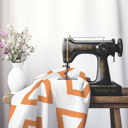 Off-White Cotton Sateen Fabric with Bold Orange Graphic , FASC-1181-391, on an antique sewing machine sitting on a desk with vase of beautiful flowers.