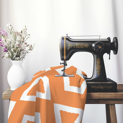 Orange Cotton Sateen Fabric with Bold Off-White Graphic , FASC-1181-392, on an antique sewing machine sitting on a desk with vase of beautiful flowers.