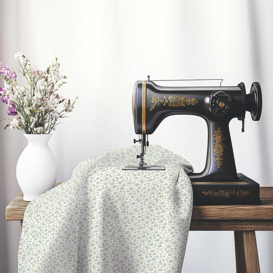 Off-White Cotton Sateen Fabric with Pale Green Hand-painted Dab Motif Print, FASC-1241-092, on an antique sewing machine sitting on a desk with vase of beautiful flowers.