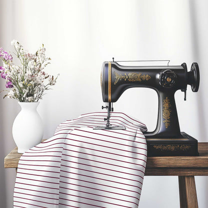 White Cotton Sateen Fabric with Fine Burgundy Red Stripes, FACS-1281-151, on an antique sewing machine sitting on a desk with vase of beautiful flowers.