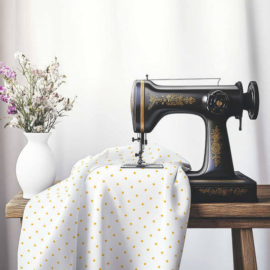 White Cotton Sateen Fabric with Yellow-Orange Diamonds, FACS-1310-101, on an antique sewing machine sitting on a desk with vase of beautiful flowers.