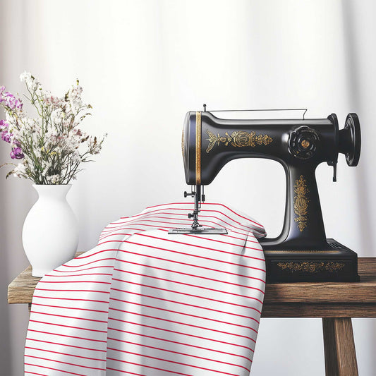 White Cotton Sateen Fabric with Fine Red Stripes, FACS-1330-151, on an antique sewing machine sitting on a desk with vase of beautiful flowers.